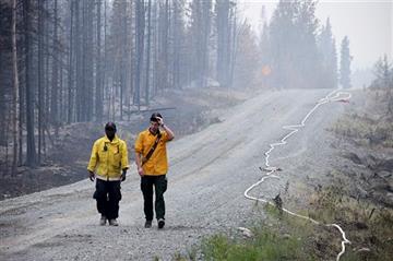 (Rashah McChesney/Peninsula Clarion via AP, File). FILE - In this June 16, 2015 file photo, two Nikiski Fire Department firefighters walk on a road near a fire-ravaged forest left behind by the Card Street fire in Sterling, Alaska. Global warming is ca...