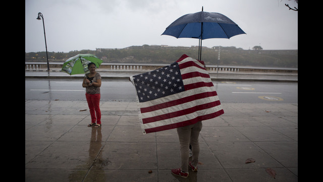 A Cuban man carrying the Stars and Stripes waits in the rain to wave to U.S. President Barack Obama's convoy as it arrives along the Malecon into Old Havana, Cuba, Sunday, March 20, 2016. (AP Photo/Rebecca Blackwell)